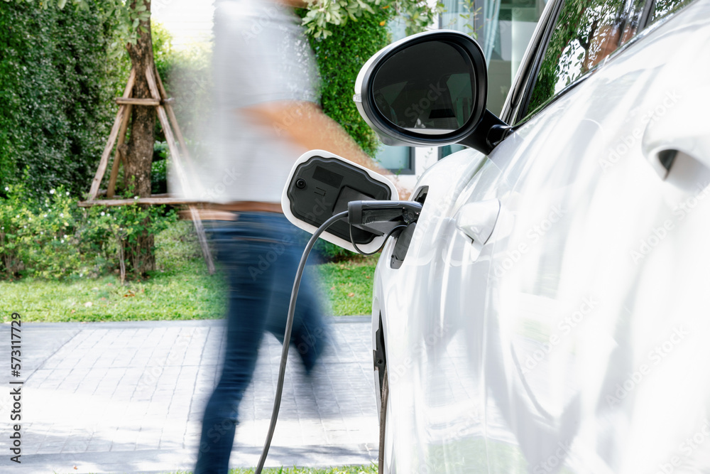 Focus recharging electric vehicle outdoor from charging station with motion blur background of man w