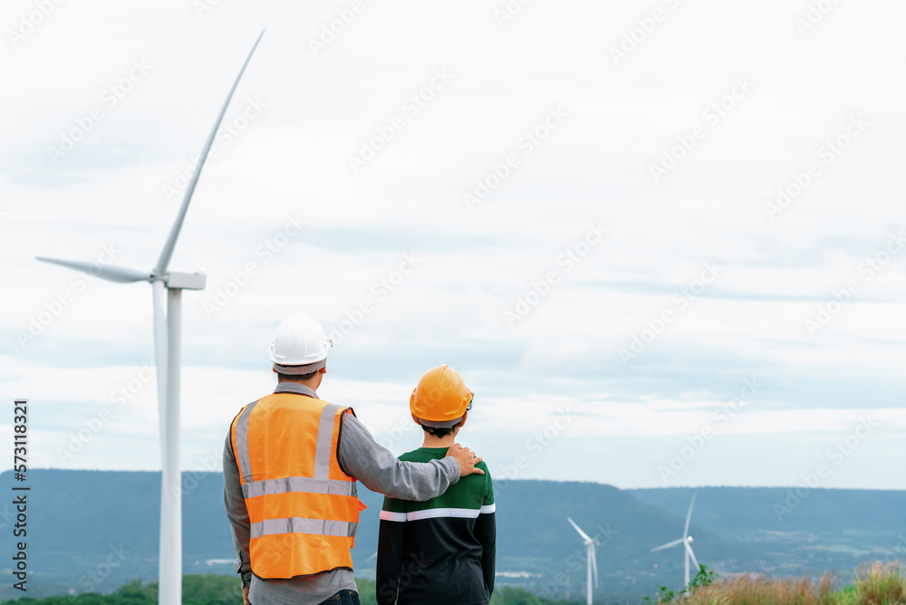 Engineer with his son on a wind farm atop a hill or mountain in the rural. Progressive ideal for the