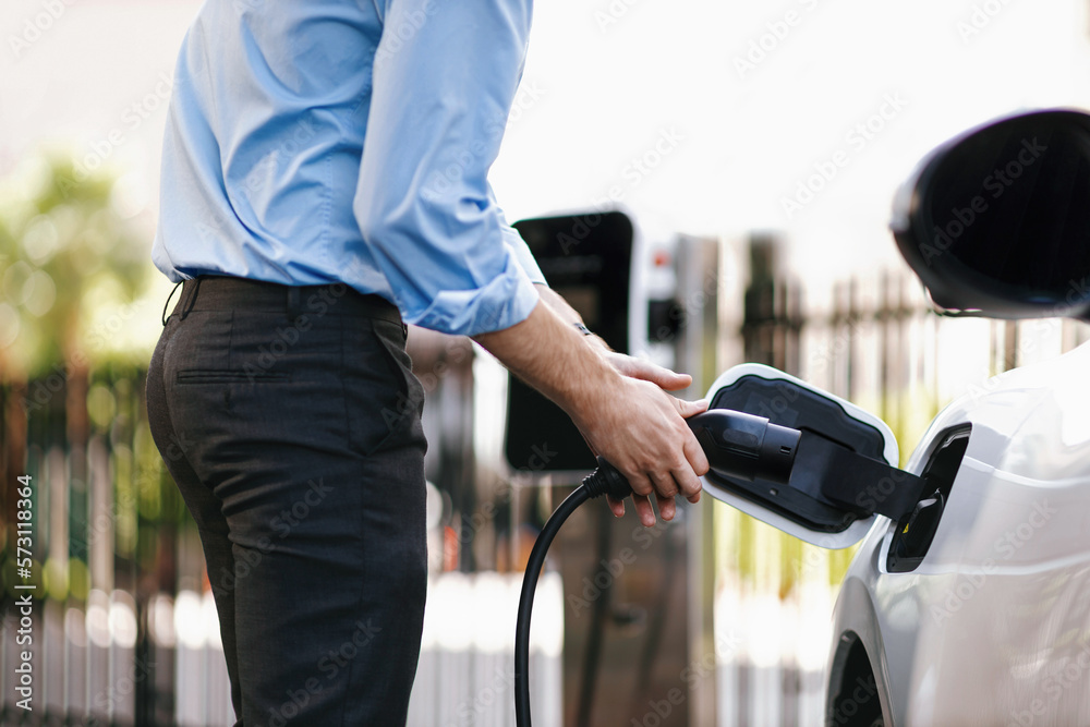 Closeup progressive man holding EV charger plug from public charging station for electric vehicle wi