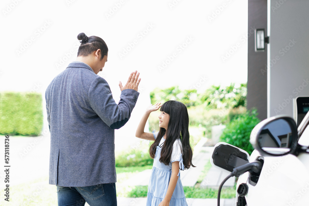 Progressive father and daughter plugs EV charger from home charging station to electric vehicle. Fut