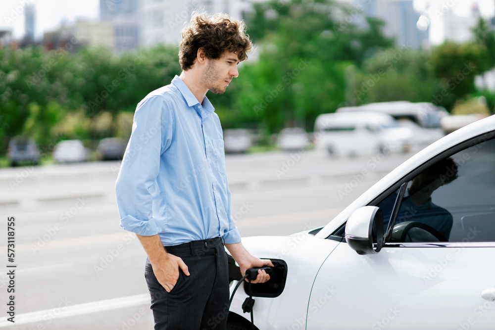 Progressive businessman insert charger plug from charging station to his electric vehicle with apart