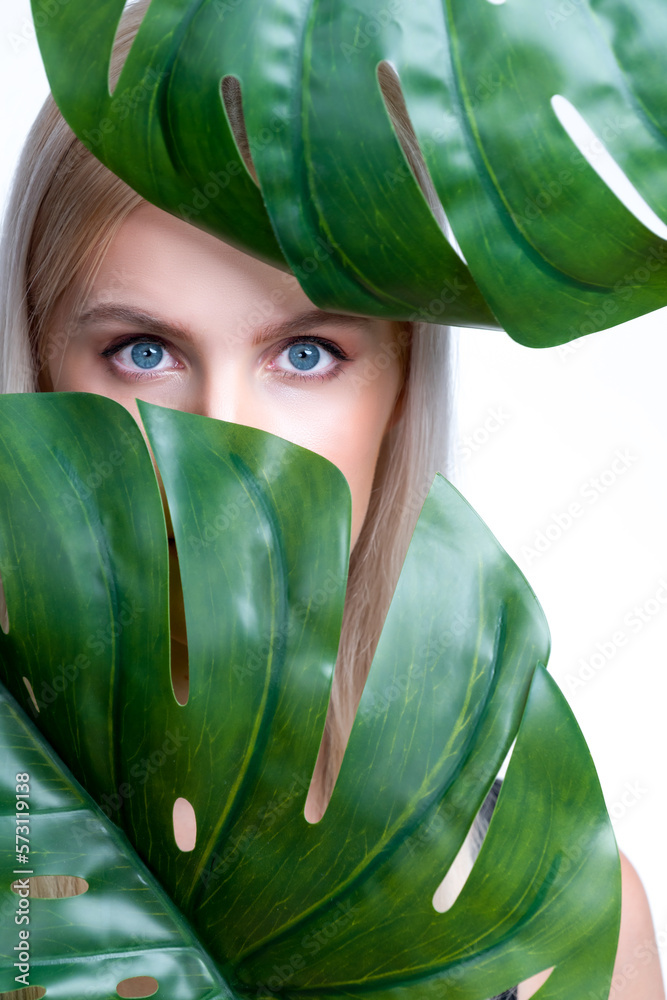 Closeup facial portrait personable woman with perfect smooth makeup holding green monstera leaves an