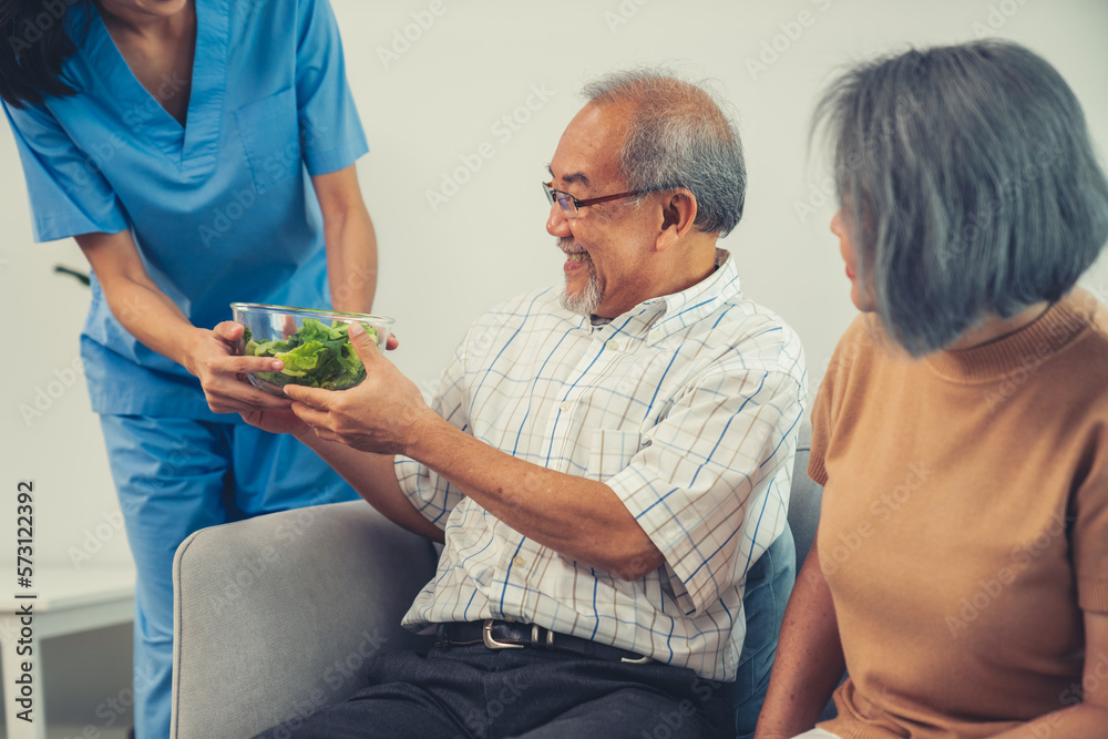 A female nurse serves a bowl of salad to a contented senior couple. Health care and medical assistan