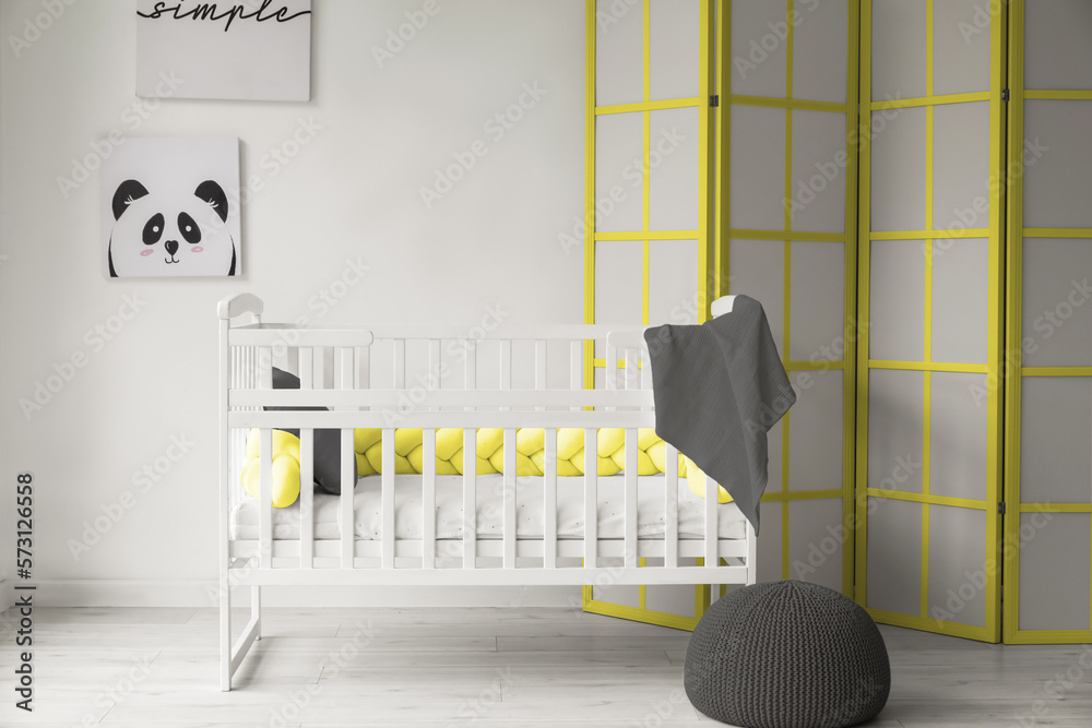 Comfortable crib and folding screen near light wall in childrens room