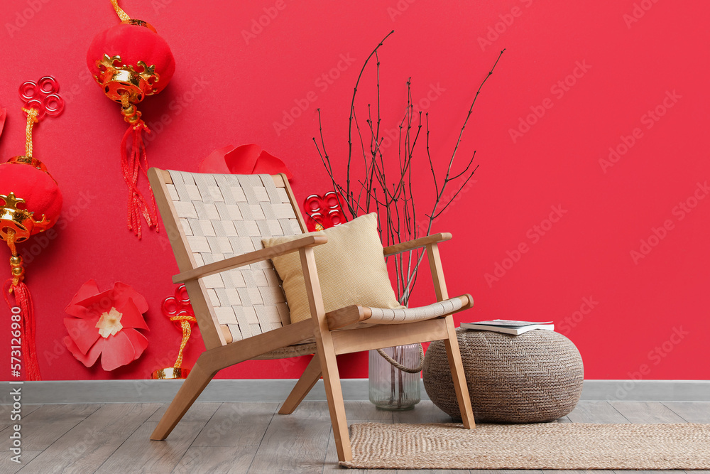 Stylish armchair and pouf near red wall with beautiful Chinese print in room