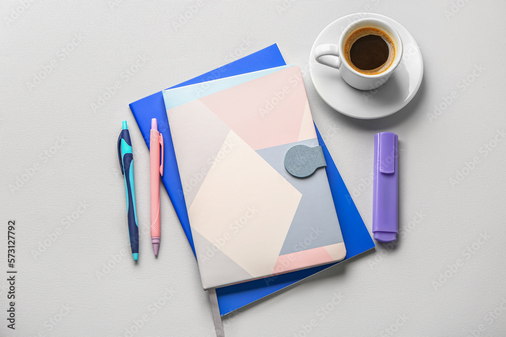 Notebooks, pens, marker and cup of coffee on light background