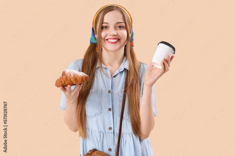 Young woman with tasty croissant and cup of coffee on beige background