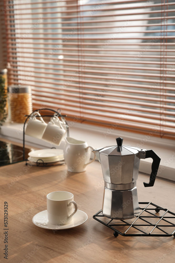 Grid with geyser coffee maker and cup on kitchen counter near window