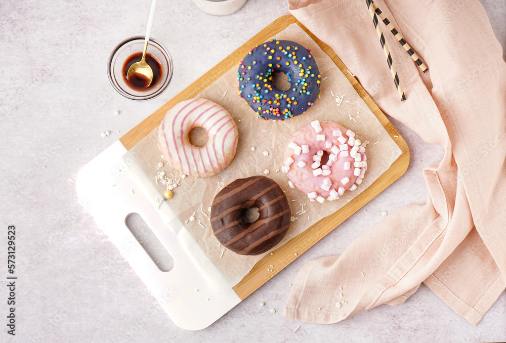 Board with different delicious donuts on white table