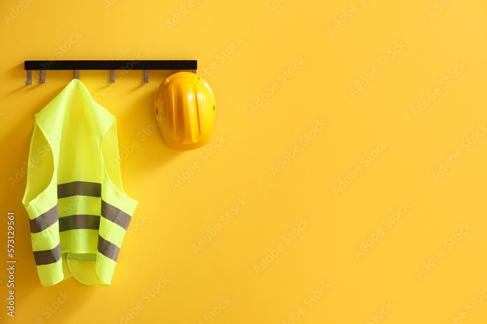 Reflective vest and hardhat hanging on yellow wall