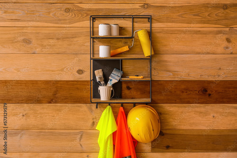 Shelf with builders supplies and reflective vests on wooden wall