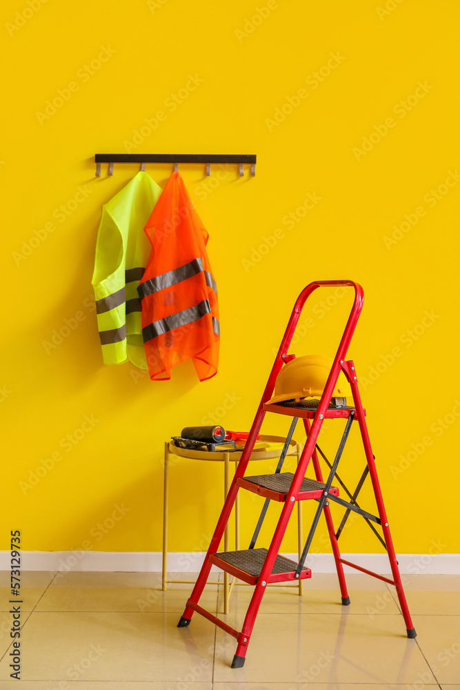 Reflective vests, stepladder and table with builders tools near yellow wall