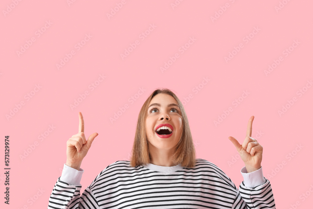 Young woman in striped sweatshirt pointing at something on pink background