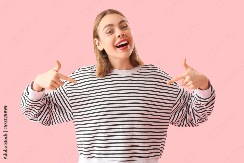 Young woman pointing at striped sweatshirt on pink background