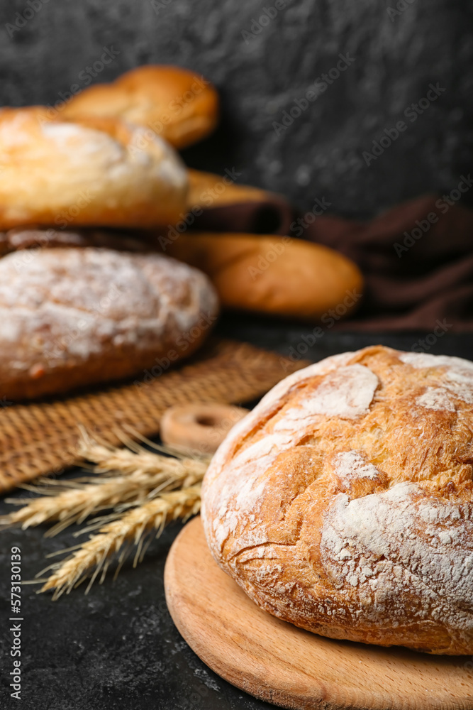 Cutting board with loaf of fresh bread and wheat ears on black table