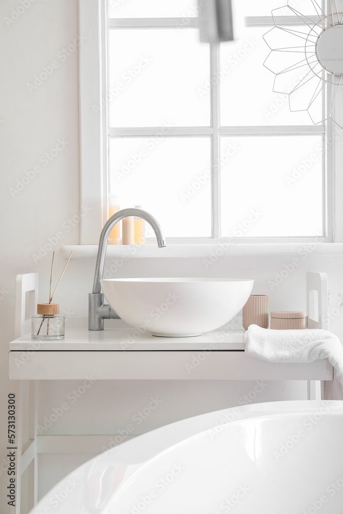 Interior of bathroom with ceramic sink and reed diffuser near window