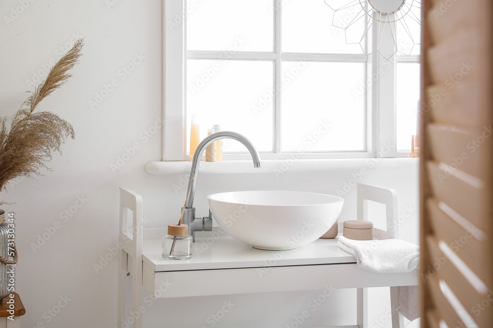 Interior of bathroom with ceramic sink and reed diffuser near window