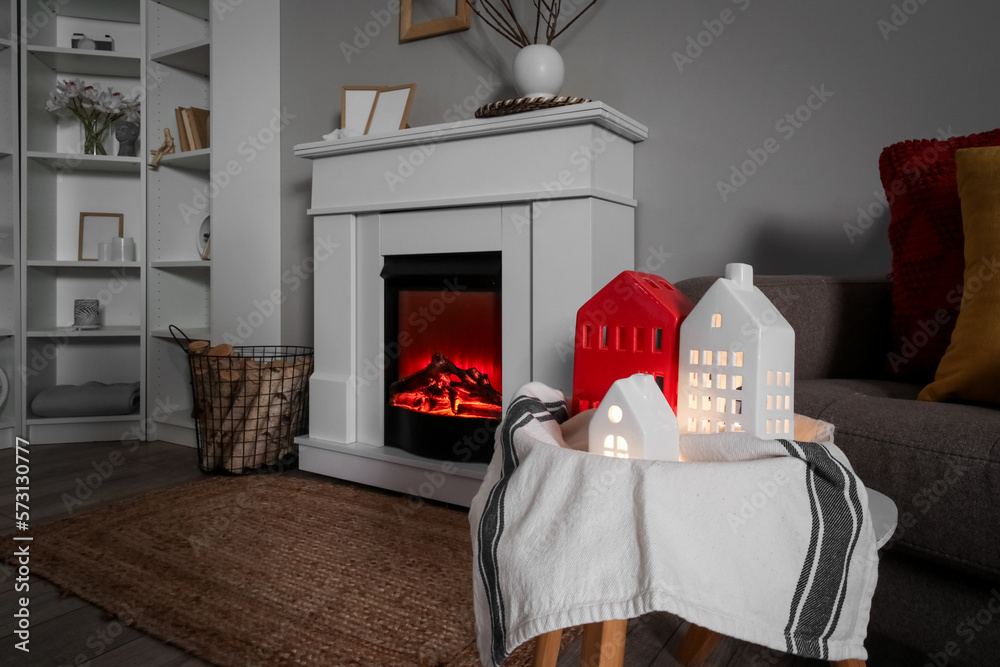 Glowing house candle holders on table near fireplace in living room