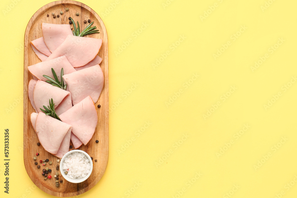 Board with slices of tasty ham, rosemary and peppercorn on yellow background