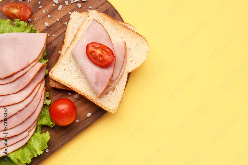 Board with slices of tasty ham, bread pieces, lettuce and tomatoes on yellow background