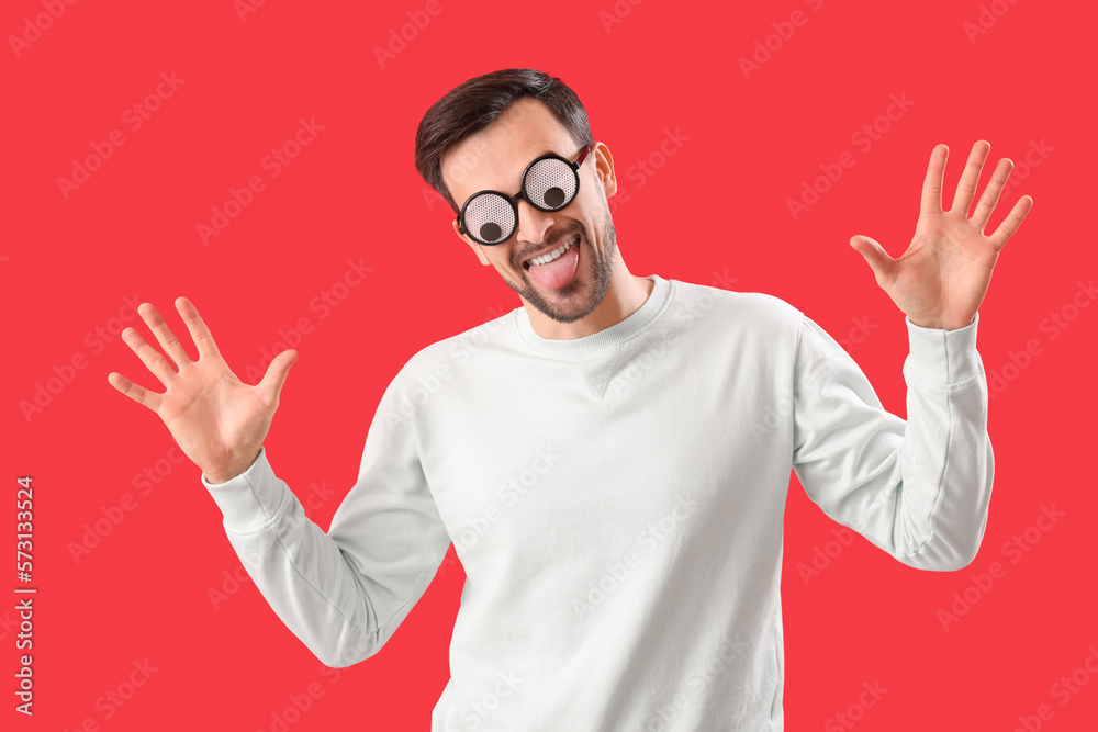 Handsome man in funny eyeglasses on red background. April Fools Day celebration