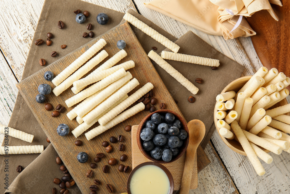 Composition with delicious wafer rolls, blueberries and coffee beans on white wooden table