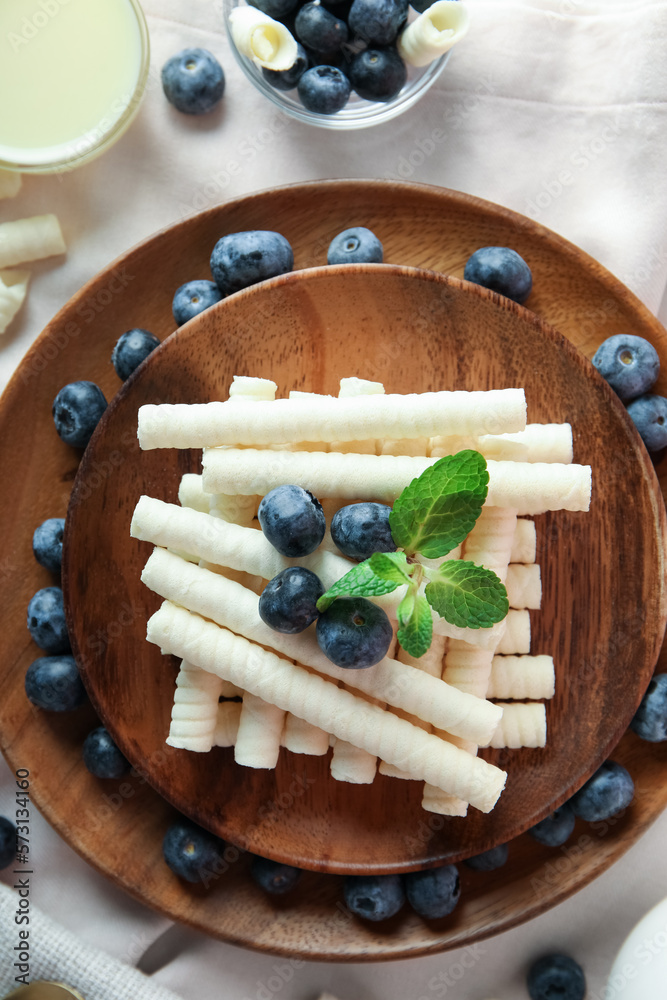 Wooden plates with delicious wafer rolls and blueberries on napkin, closeup