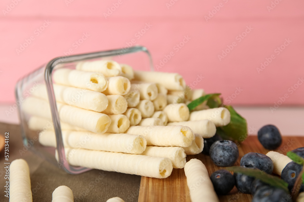 Overturned bowl of delicious wafer rolls and blueberries on table near pink wall