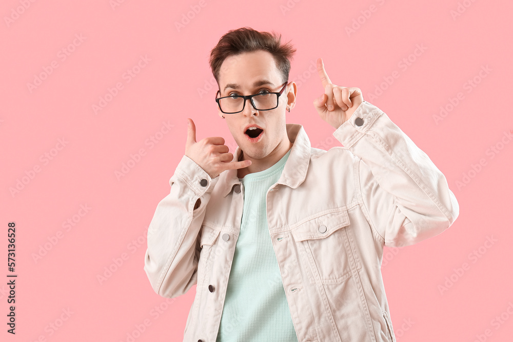 Surprised young man with raised index finger showing  call me  gesture on pink background