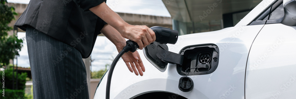 Closeup progressive suit-clad businesswoman with her electric vehicle recharge her car on public cha