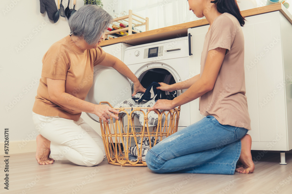 Daughter and mother working together to complete their household chores near the washing machine in 