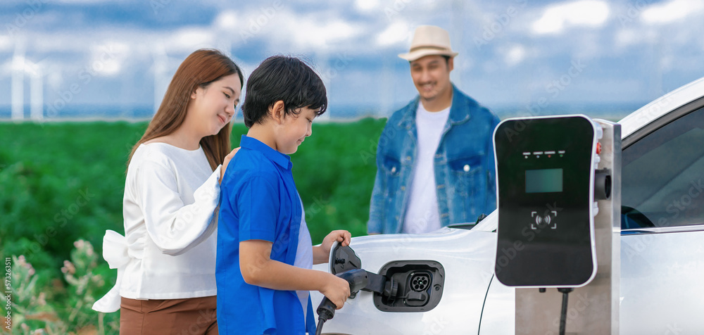 Concept of progressive happy family enjoying their time at wind farm with electric vehicle. Electric