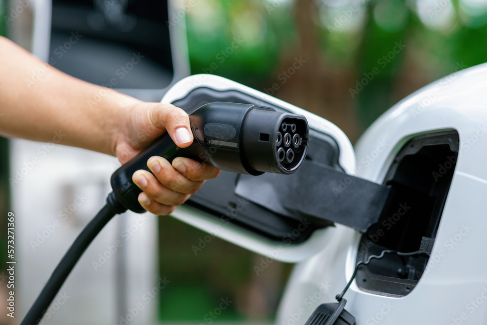 Hand inserting EV charging plug to electric vehicle in focus shot with blurred background of outdoor