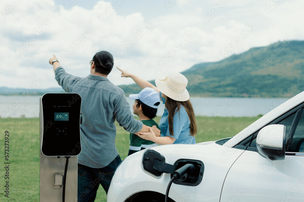 Concept of progressive happy family enjoying their time at green field and lake with electric vehicl