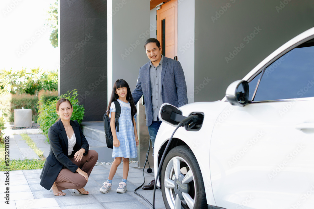 Progressive young parents and daughter with electric vehicle and home charging station. Green and cl