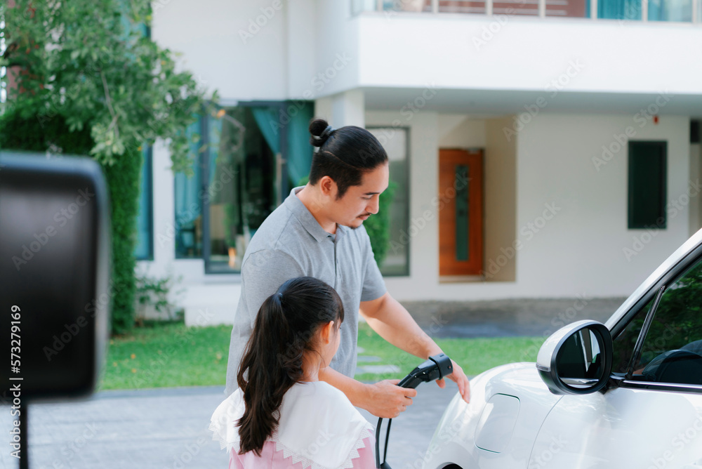 Progressive father and daughter returned from school in electric vehicle that is being charged at ho