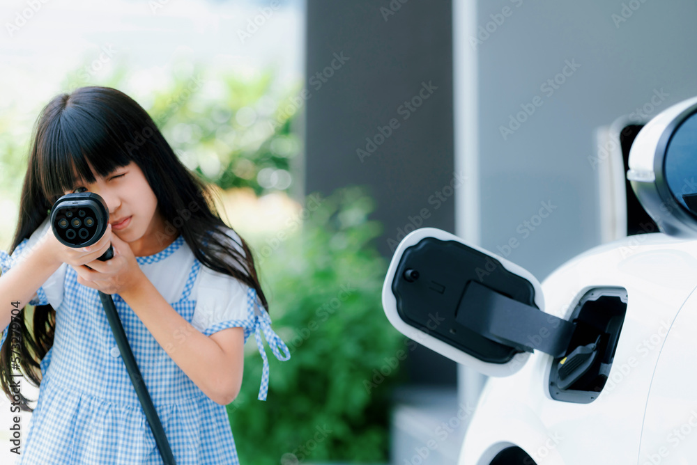 A playful girl holding and pointing an EV plug, a home charging station providing a sustainable powe