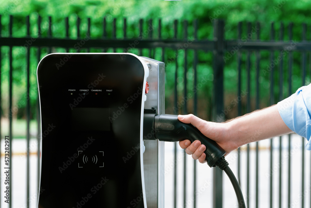 Closeup progressive man holding EV charger plug from public charging station for electric vehicle wi