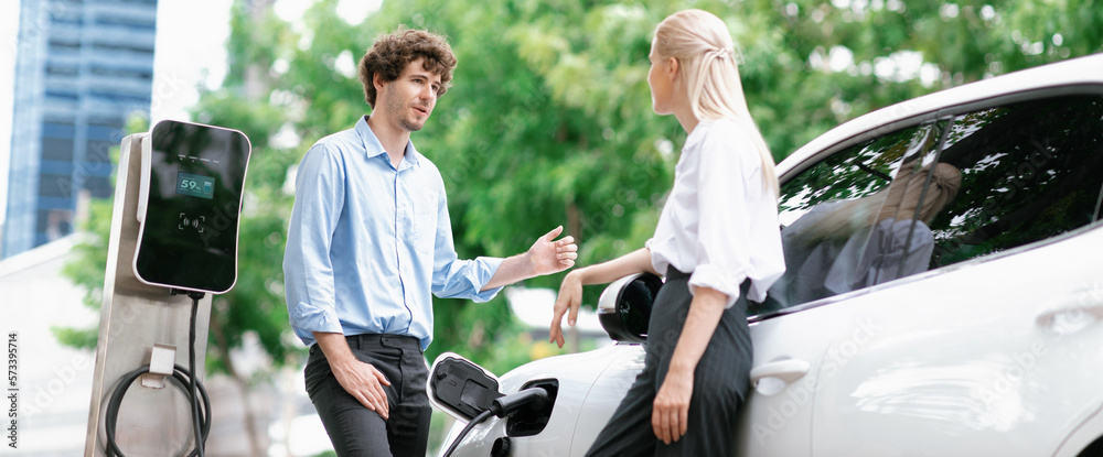 Progressive businessman and businesswoman with electric car parking and connected to public charging