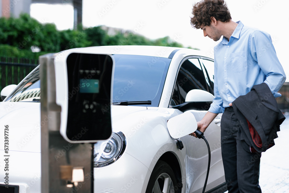 Progressive businessman insert charger plug from charging station to his electric vehicle with apart