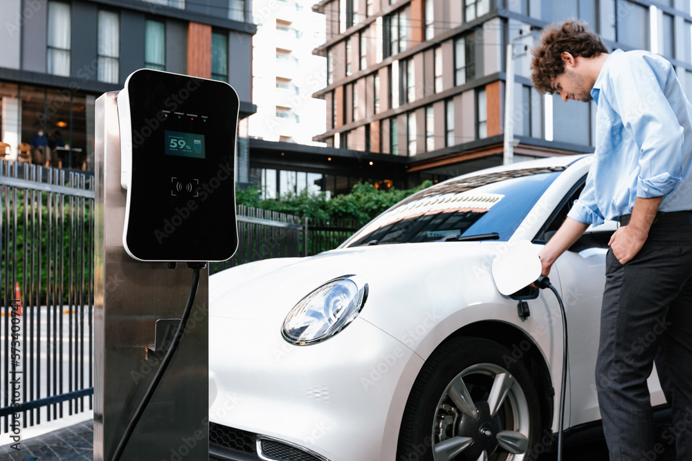 Progressive businessman insert charger plug from charging station to his electric vehicle with apart