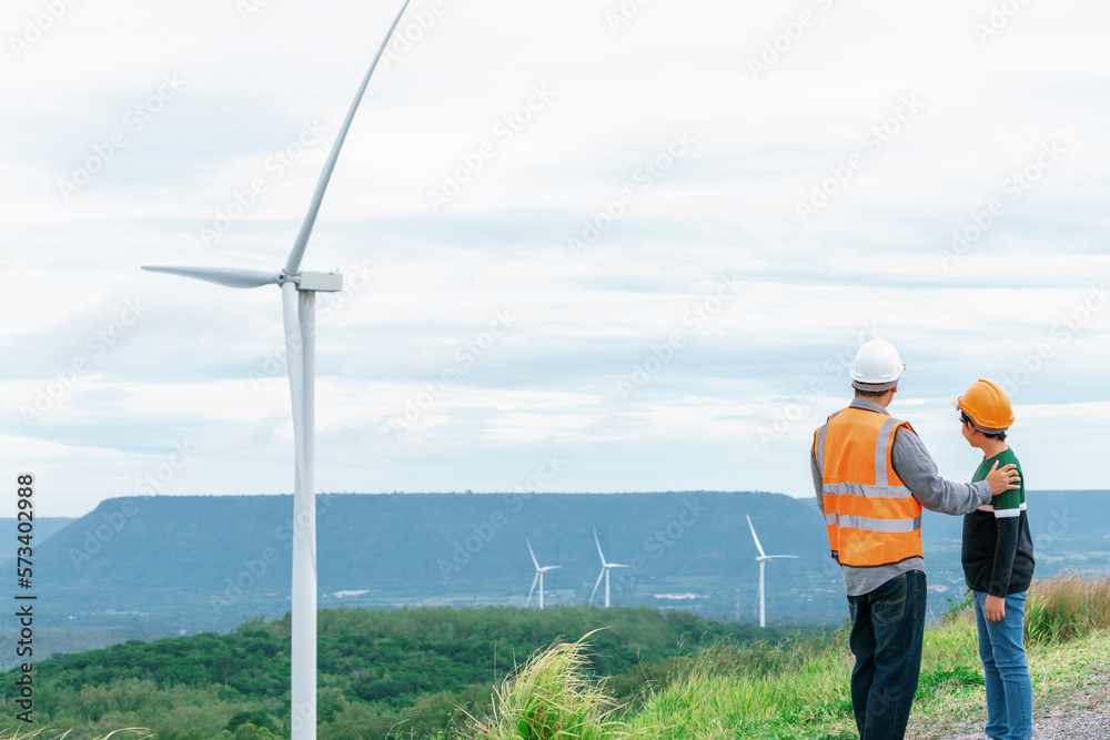 Engineer with his son on a wind farm atop a hill or mountain in the rural. Progressive ideal for the