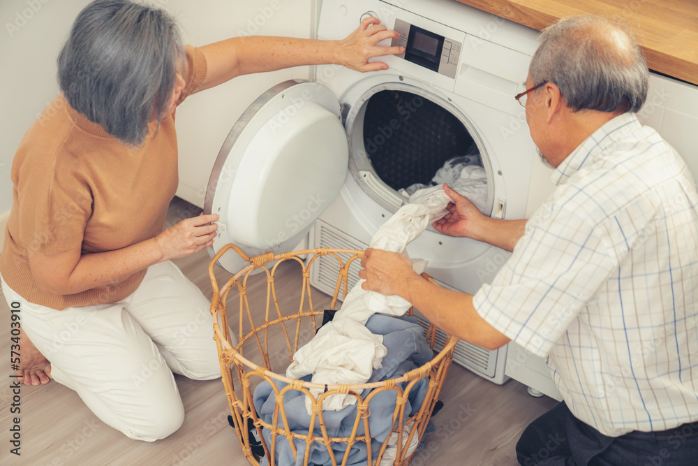 Senior couple working together to complete their household chores at the washing machine in a happy 