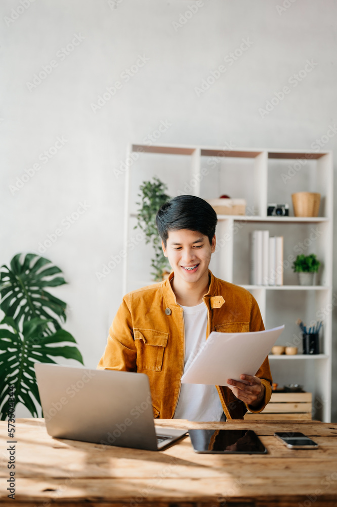 Young business man working at home office with laptop, tablet and taking notes on the paper.