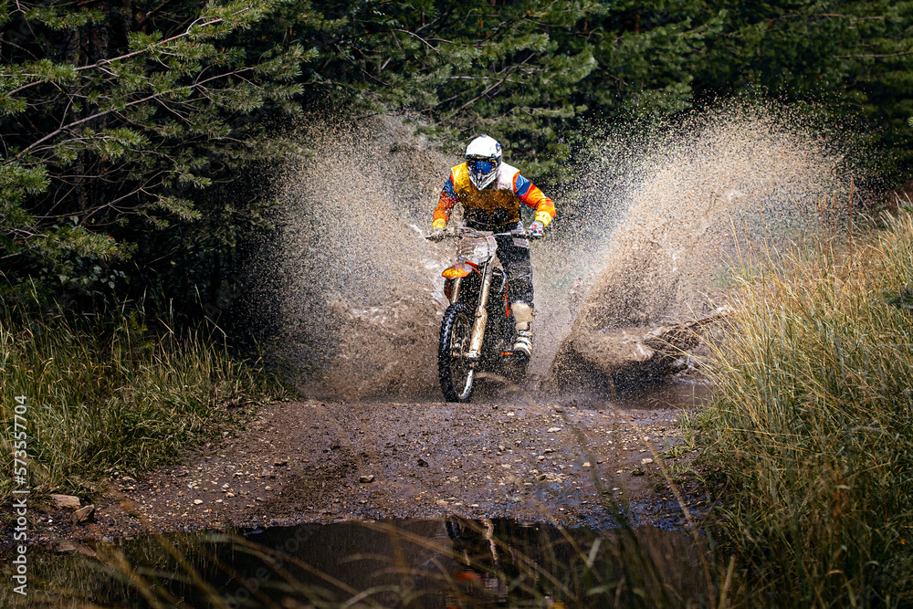 enduro racer riding on water with splashes motocross race in forest