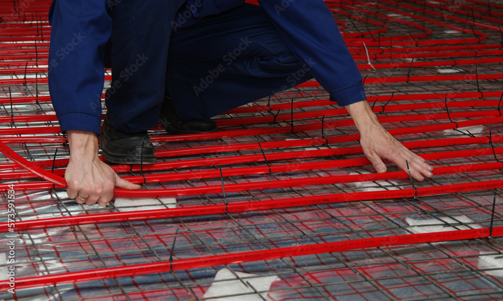 Worker is installing a red pipe for underfloor heating