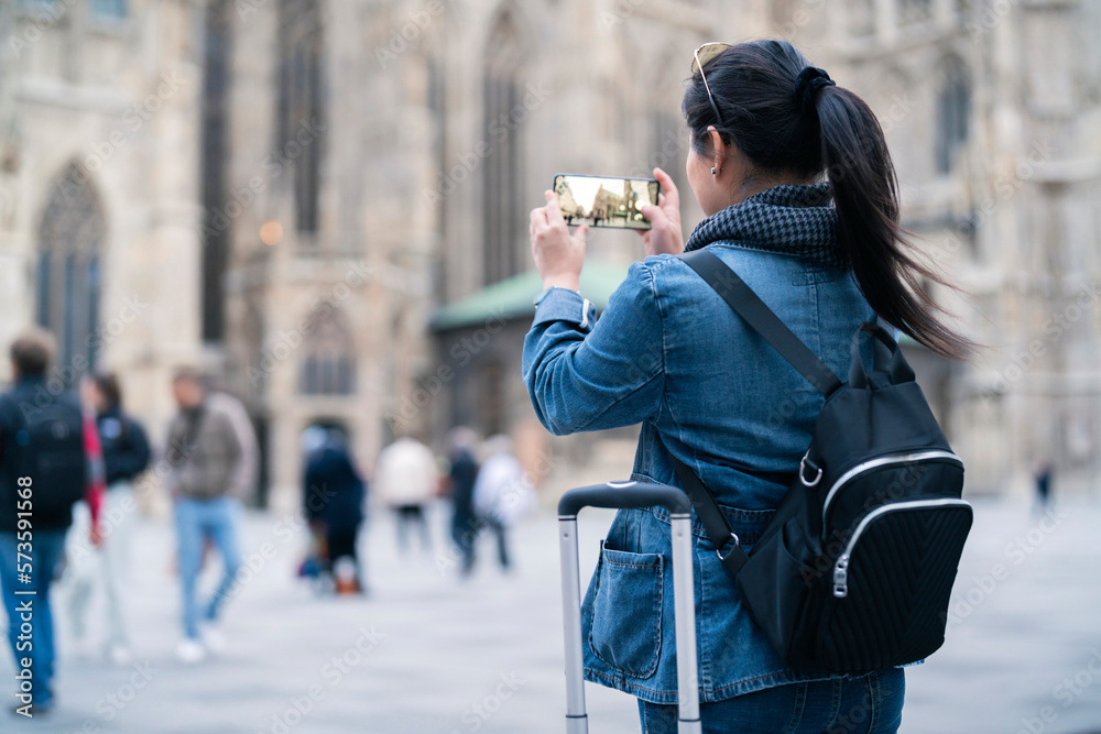 smiling asian female traveller using smartphone taking photo of vienna Austria famous church with le