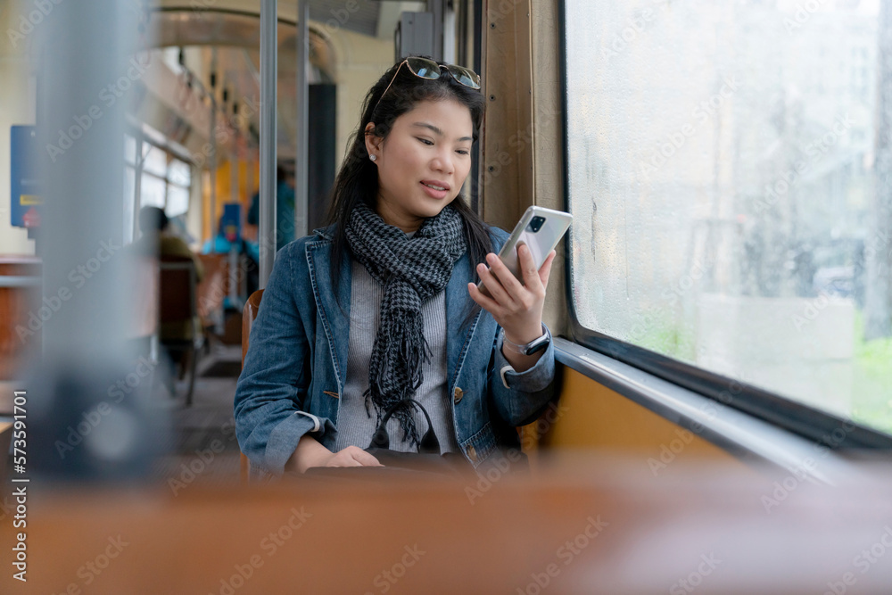 Young and happy asian female woman using smartphone while sitting near the window in the public tran