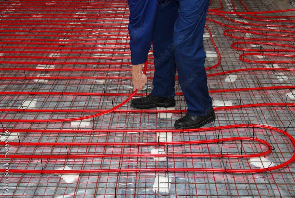 Worker is installing a red pipe for underfloor heating