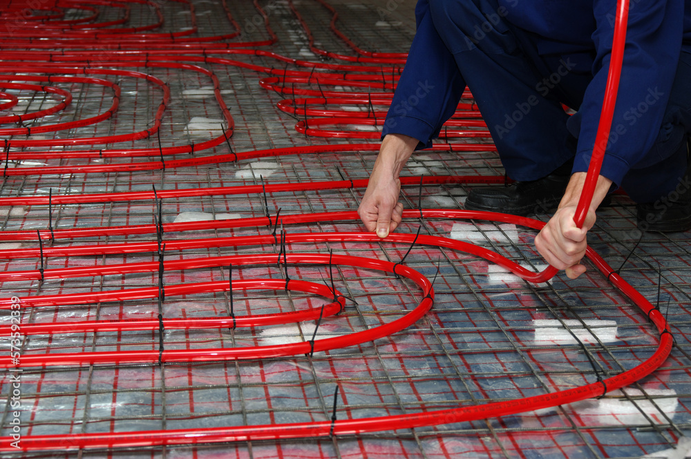 Worker is installing a red pipe for underfloor heating